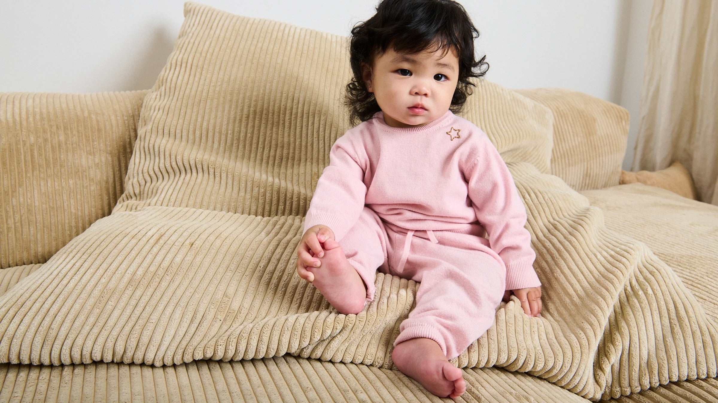 Girl sitting on the couch with a pink sweater and pant set holding her foot.