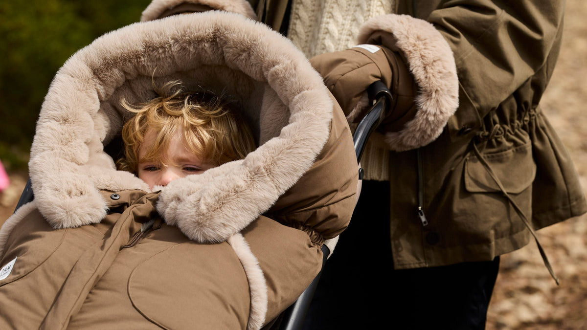 Mother wearing 7AM warmmuffs and pushing a stroller with a baby in the 7AM Enfant blanket 212 footmuff