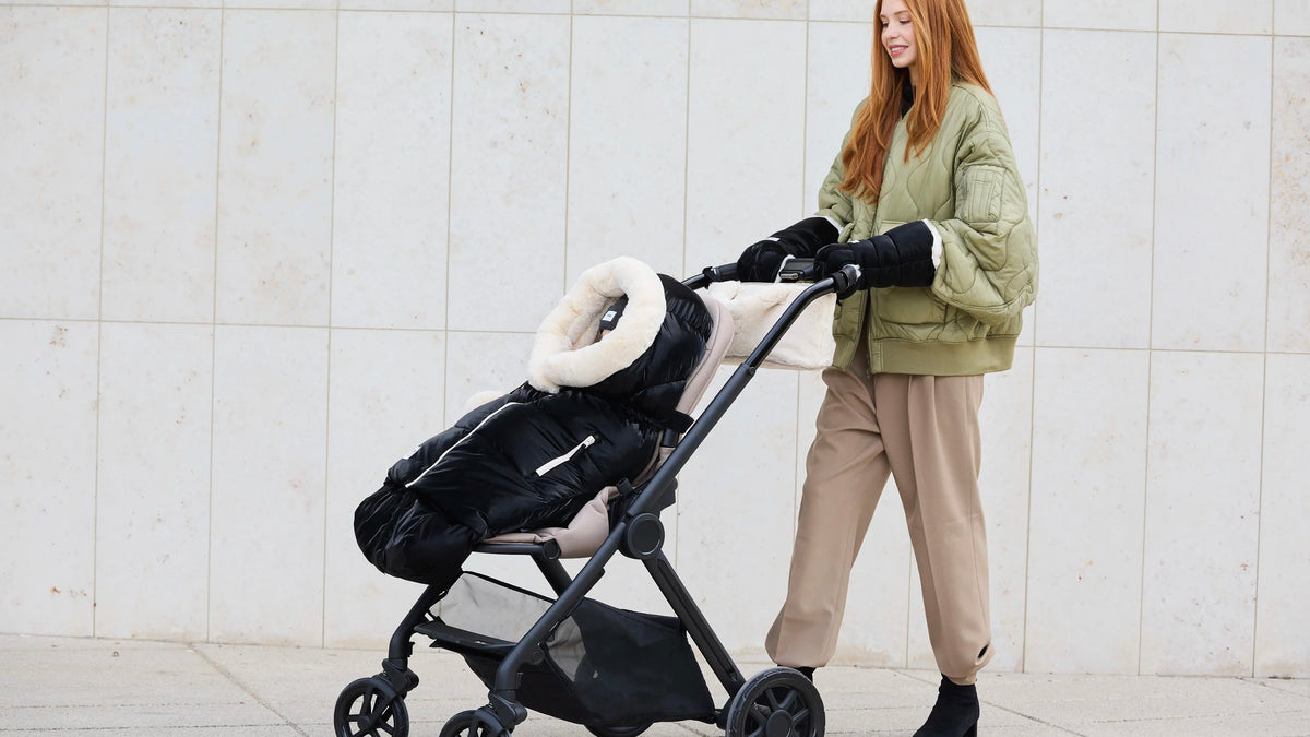 Woman in green jacket is pushing a black stroller with a 7AM product in the stroller and baby inside it.