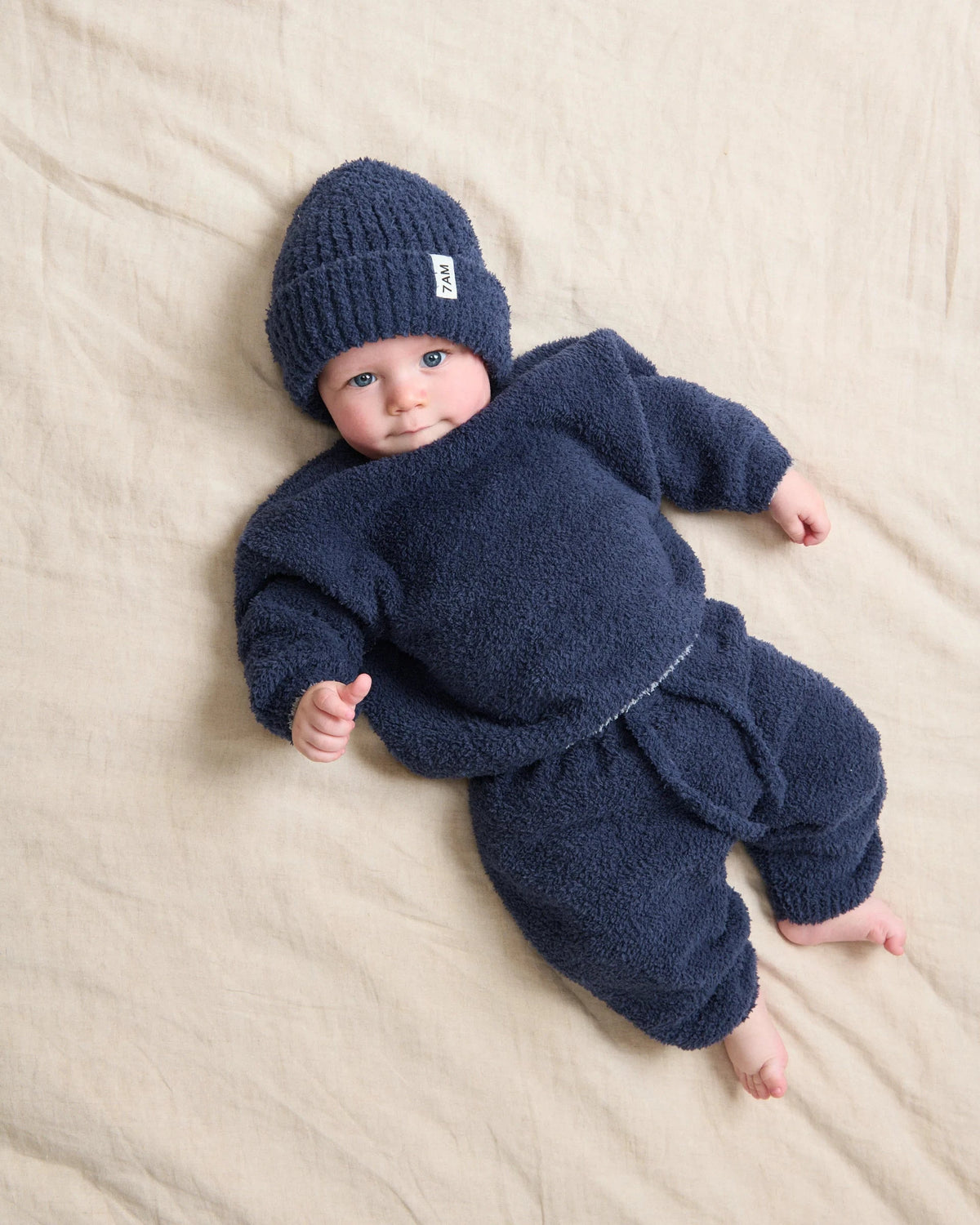 Baby wearing a navy blue outfit and hat on a beige blanket