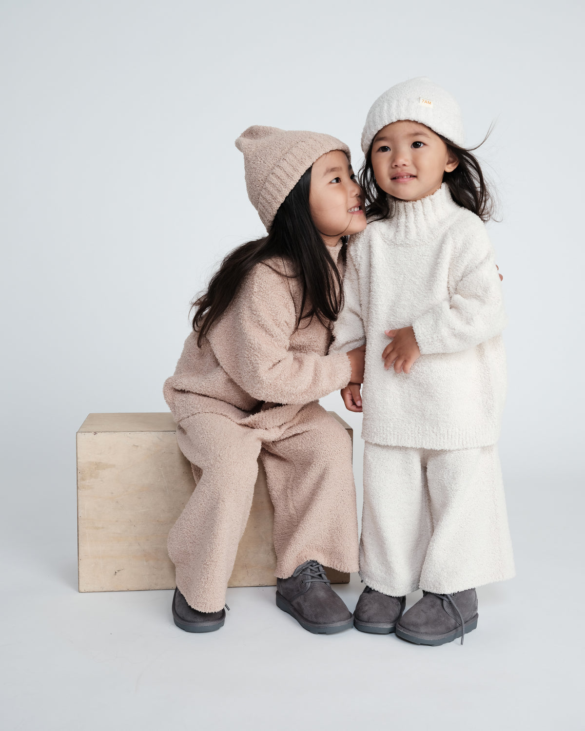 Two children in matching outfits with hats on a white background