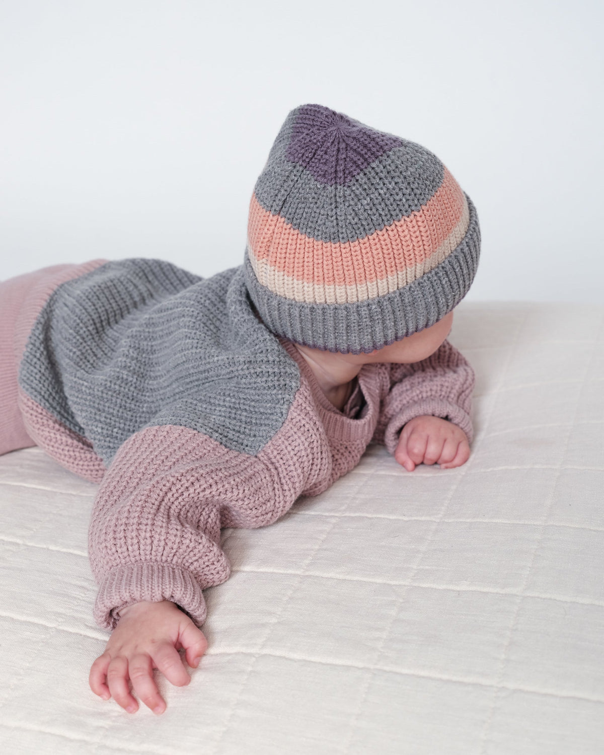 Baby wearing a knitted outfit with a striped hat on a white background
