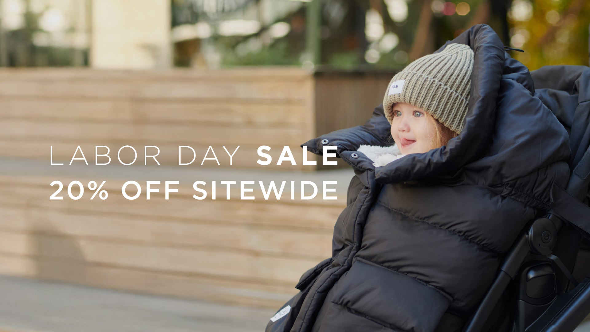 Image of a kid covered with a footmuff attached to the stroller, text overlay says "labor day sale 20% sitewide"